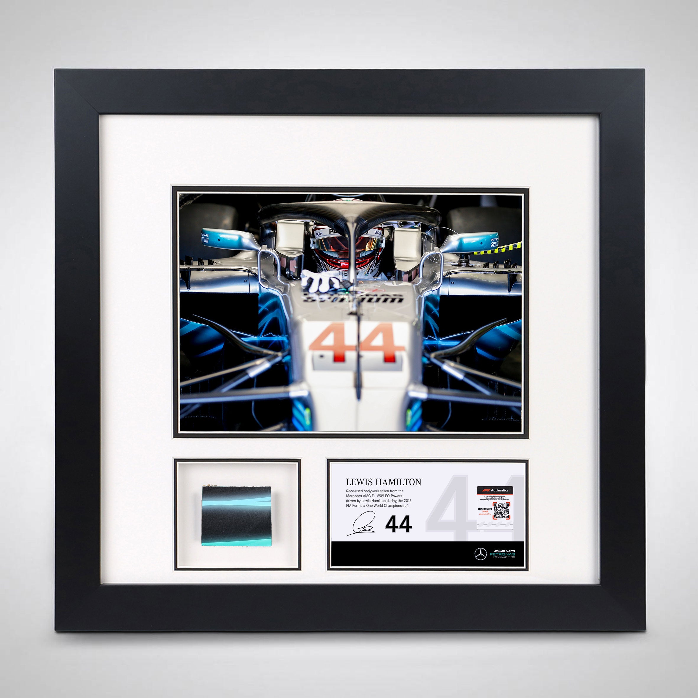 Picture frame with a peice of Lewis Hamilton's Mercedes race car below a picture of him in the car.